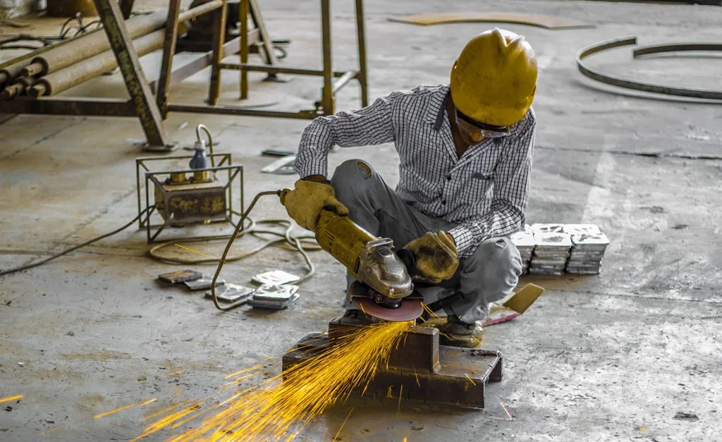 A worker grinds metal, creating a shower of sparks in a workshop